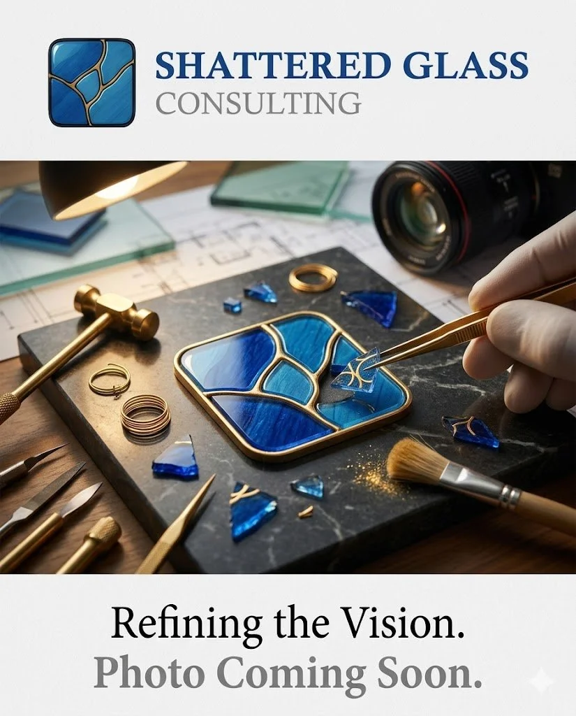 Logo of Shattered Glass Consulting with a blue shattered glass icon and the company name. Behind it, a workspace with stained glass art in progress, tools, blue glass pieces, a camera, and a hand working on the glass.