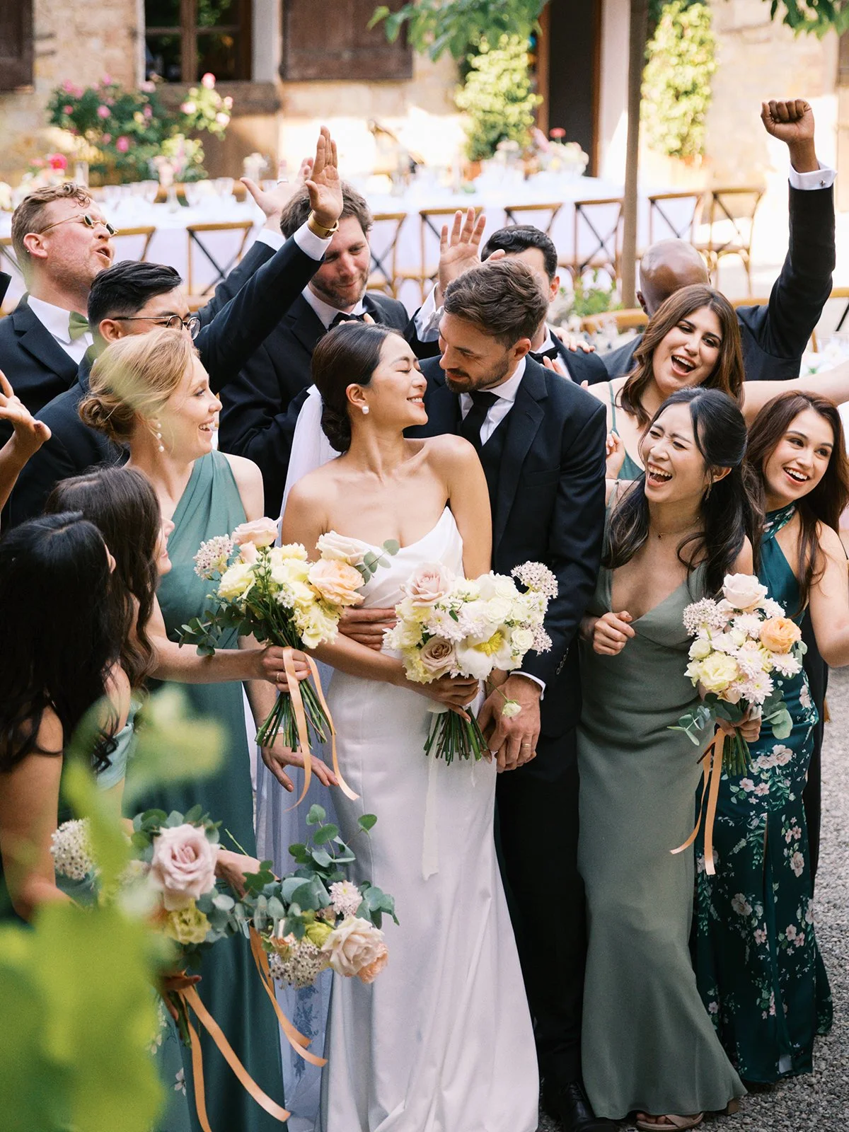 Wedding celebration with bride and groom surrounded by guests holding bouquets, celebrating outdoors.