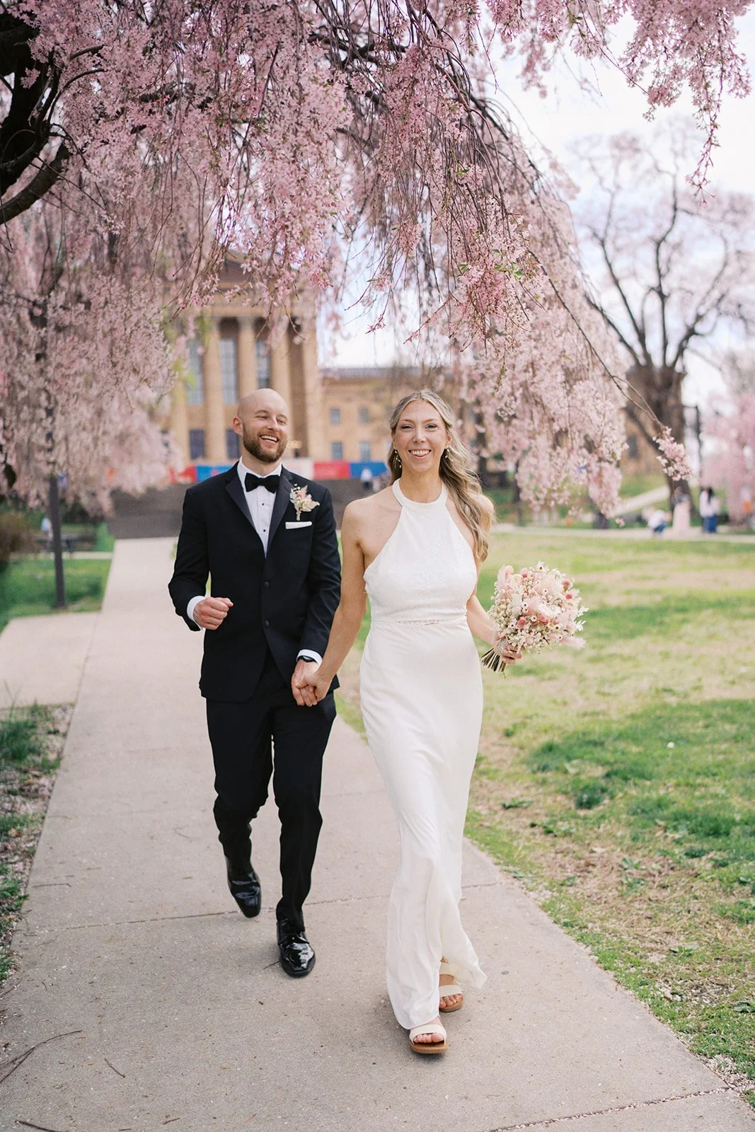couple hand in hand beneath cherry blossoms in philadelphia's fairmount park