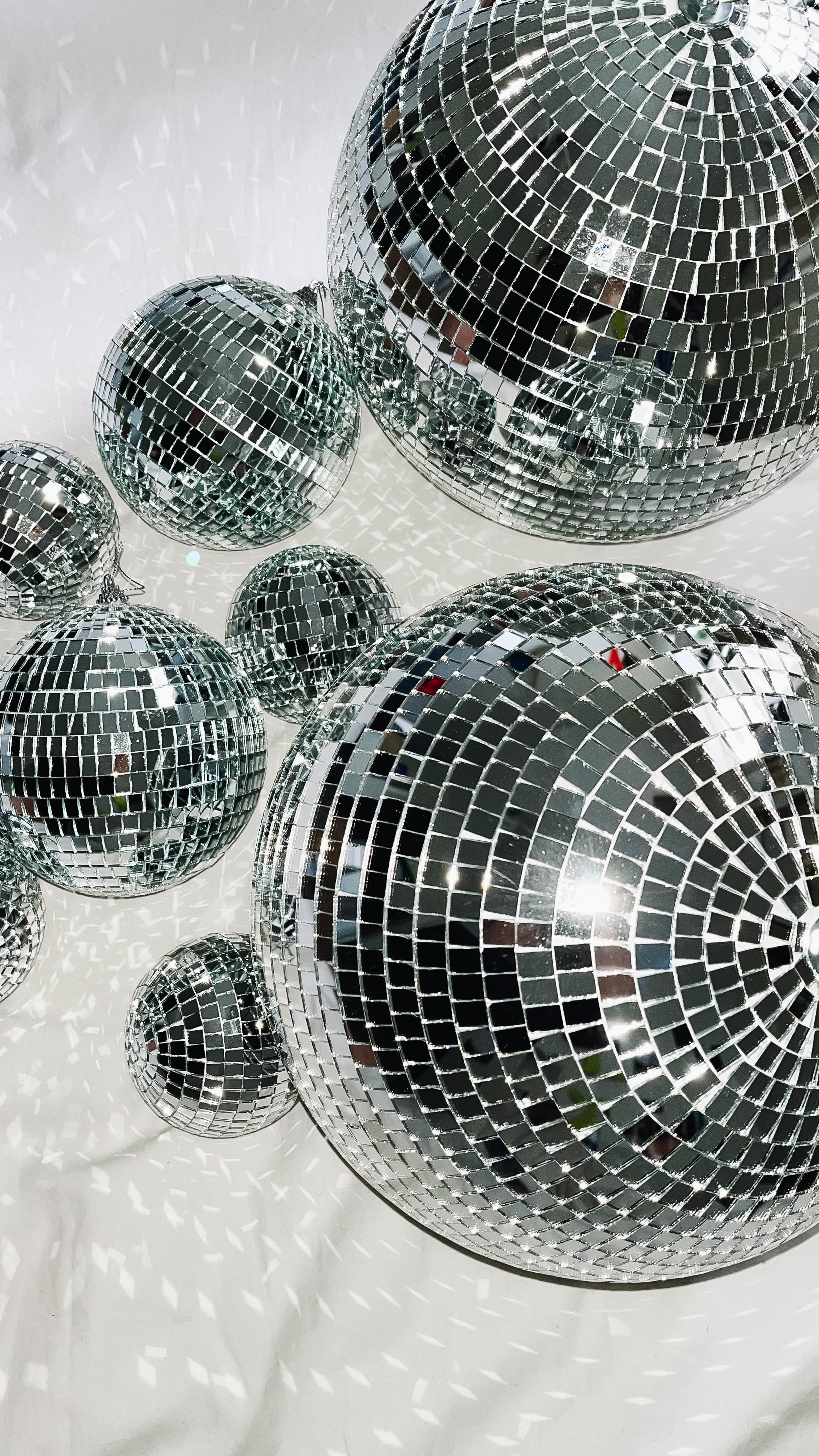 Multiple disco balls of various sizes hanging from the ceiling, reflecting light and casting patterned shadows on the white surface below.