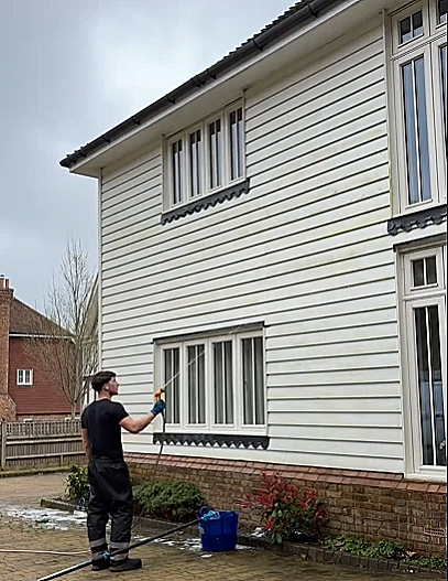 Man cleaning the exterior of a white, two-story house with a power washer.