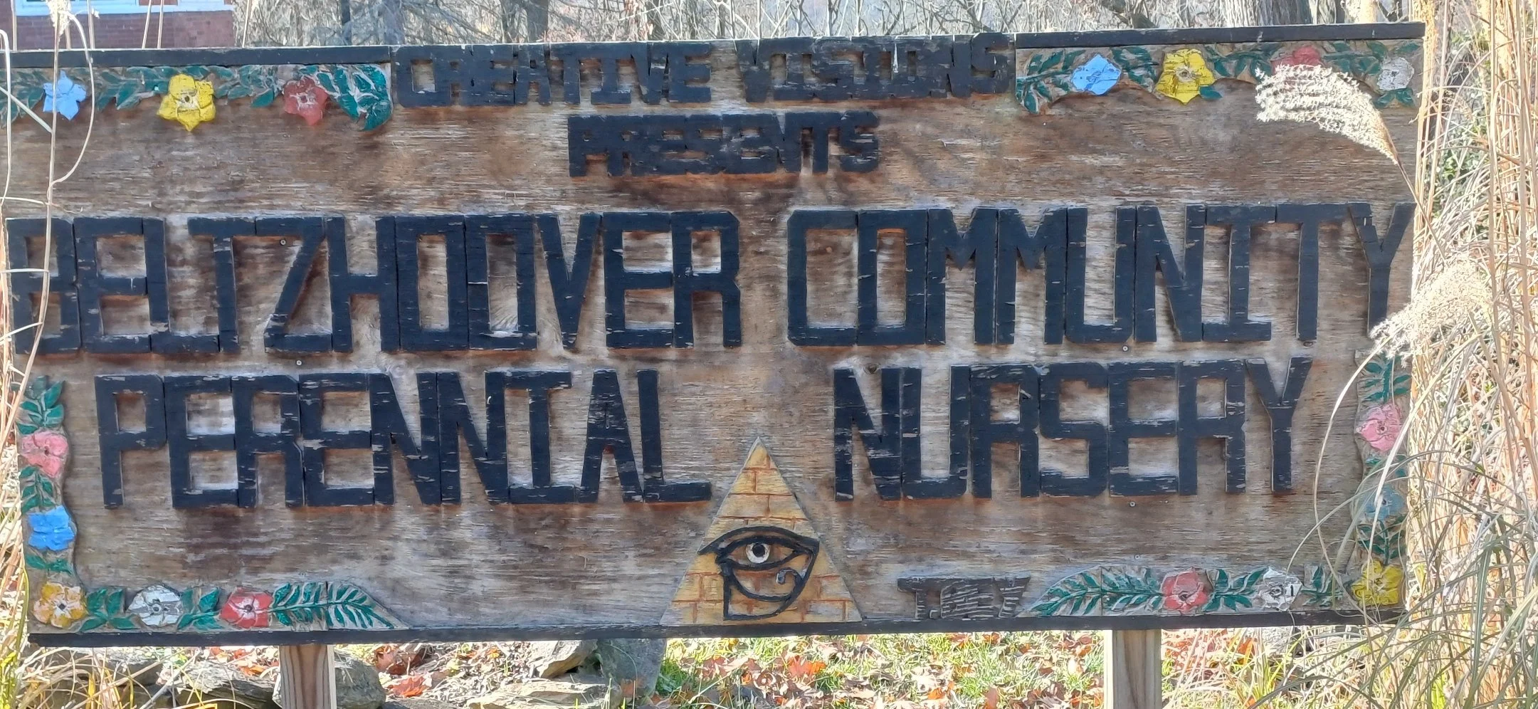 Wooden sign for the Beltzhoover Community Paternity Nursery, decorated with painted flowers and a pyramid with an eye in the center.