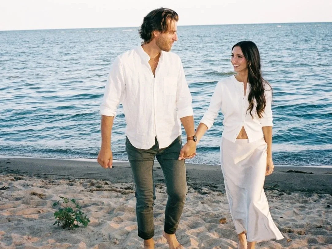 A man and woman holding hands and walking on a beach.