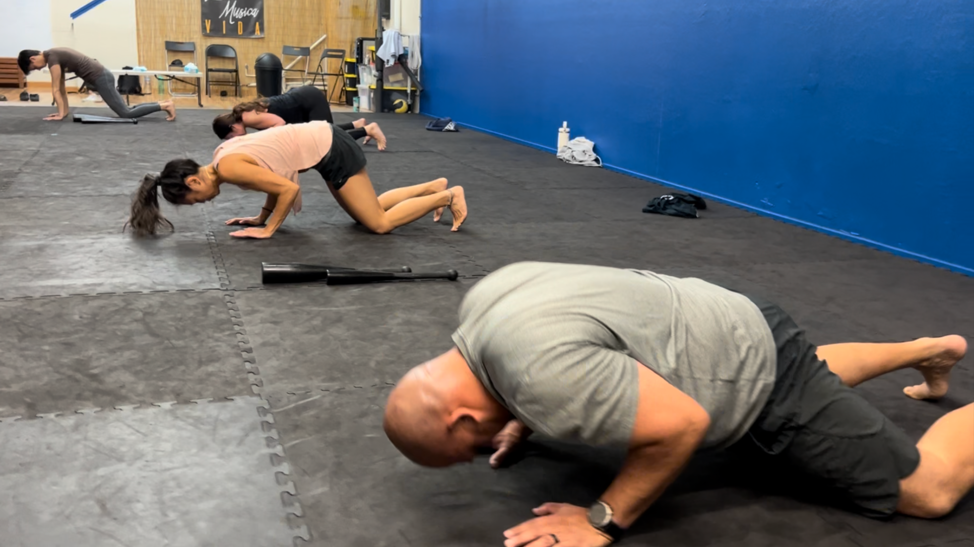 People doing push-ups on a black mat in a gym.