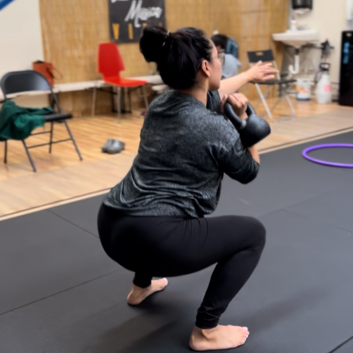 Woman in a gym doing a squat while holding a kettlebell