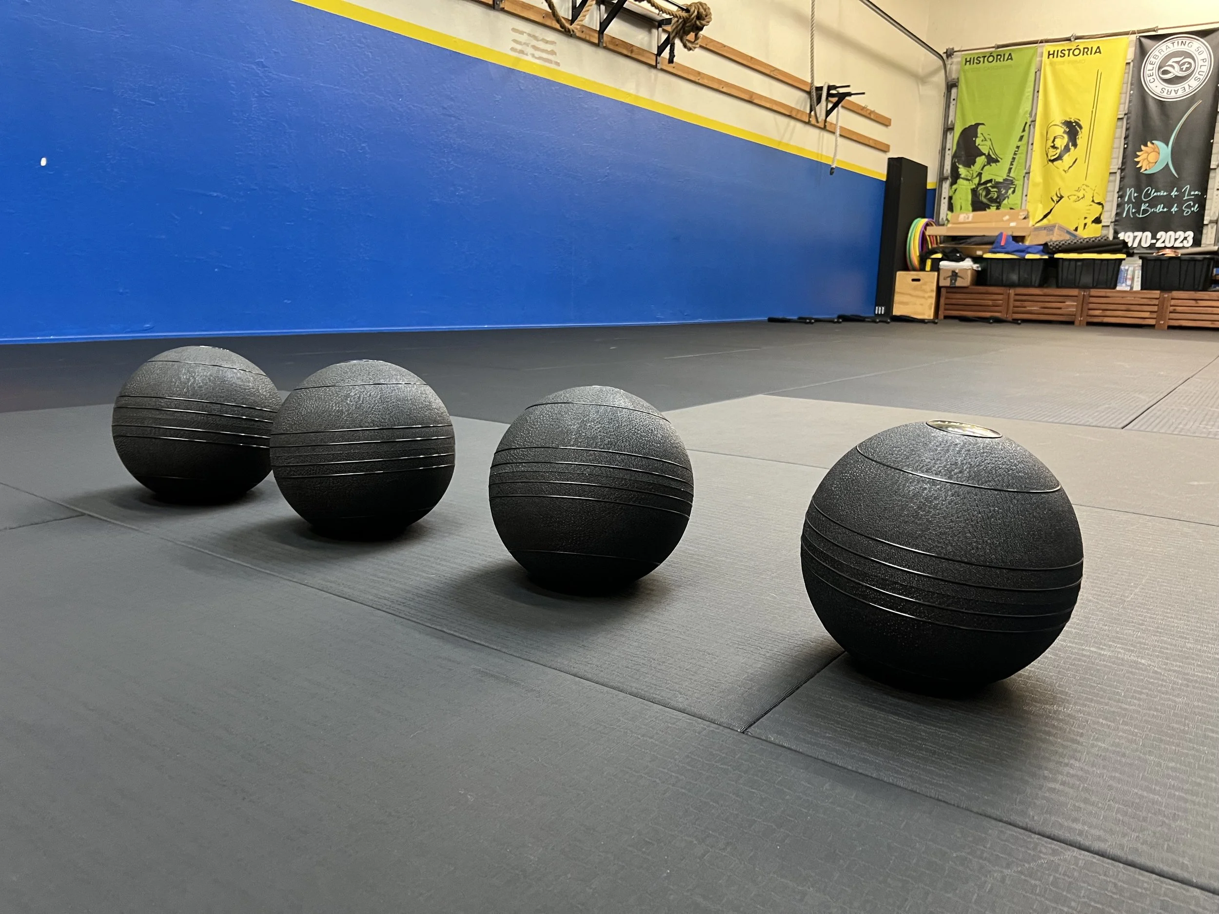 Four black exercise balls lined up on a dark gym floor