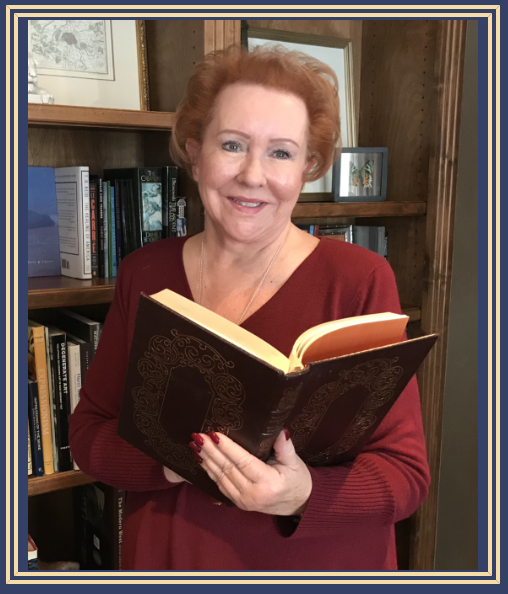 Judy Goodman wearing a red sweater, holding an open book in a room with wooden bookshelves filled with books.