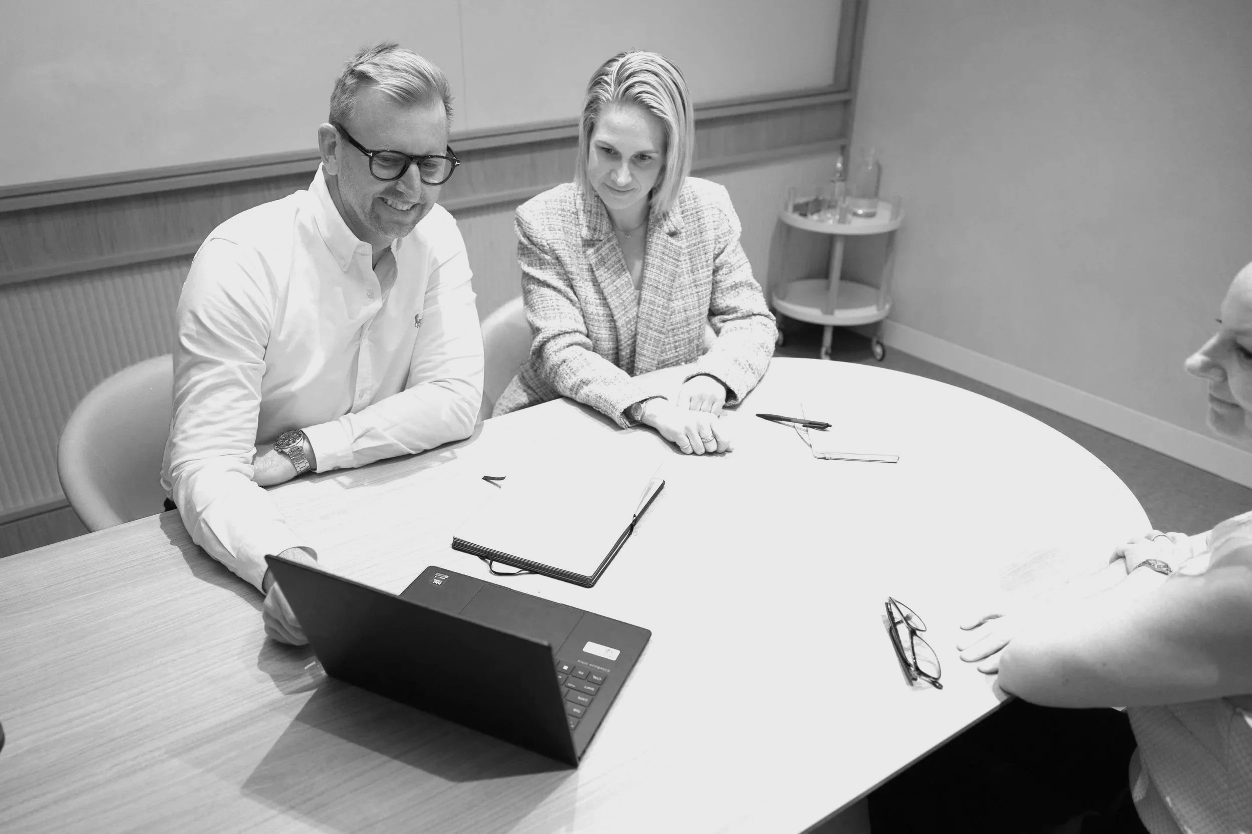 Four people sitting around a conference table having a meeting, with a laptop, notebooks, and pens.