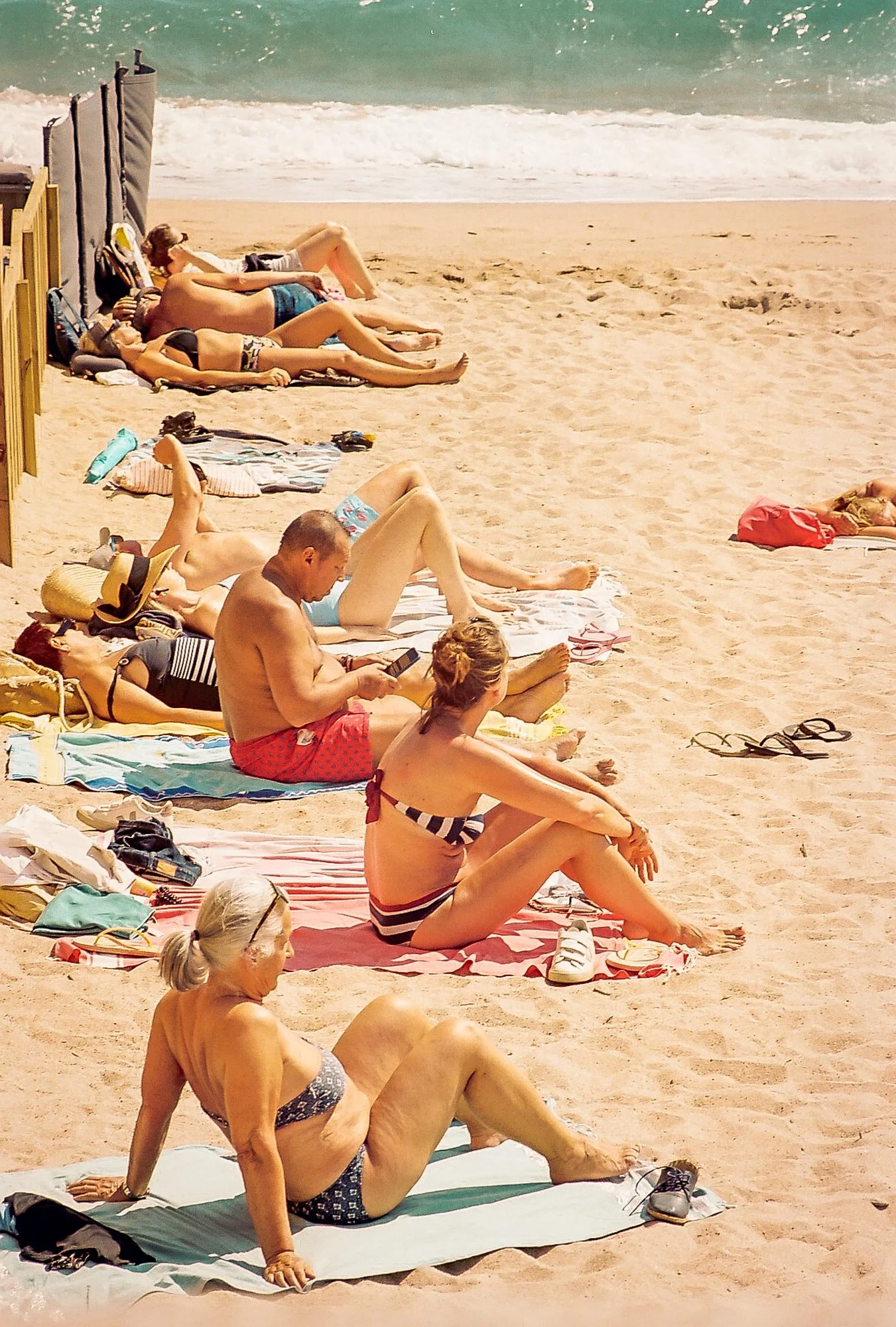 People sunbathing and relaxing on towels on a sandy beach near the ocean.