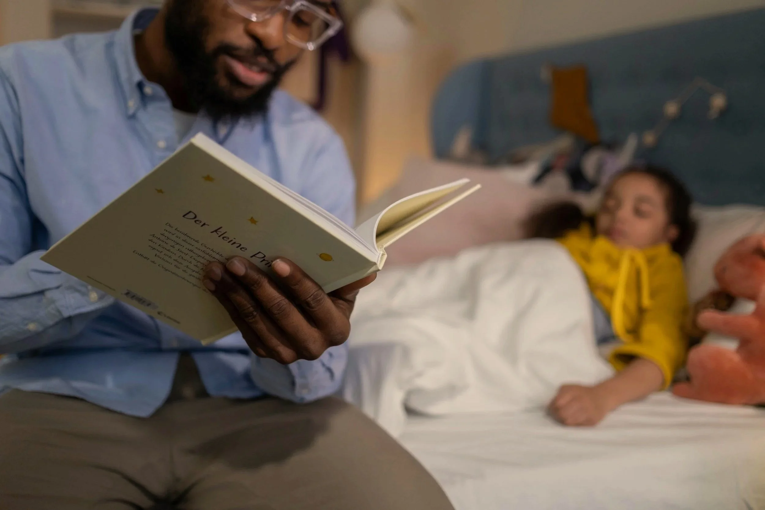 Adult reading a story to a little girl tucked into bed