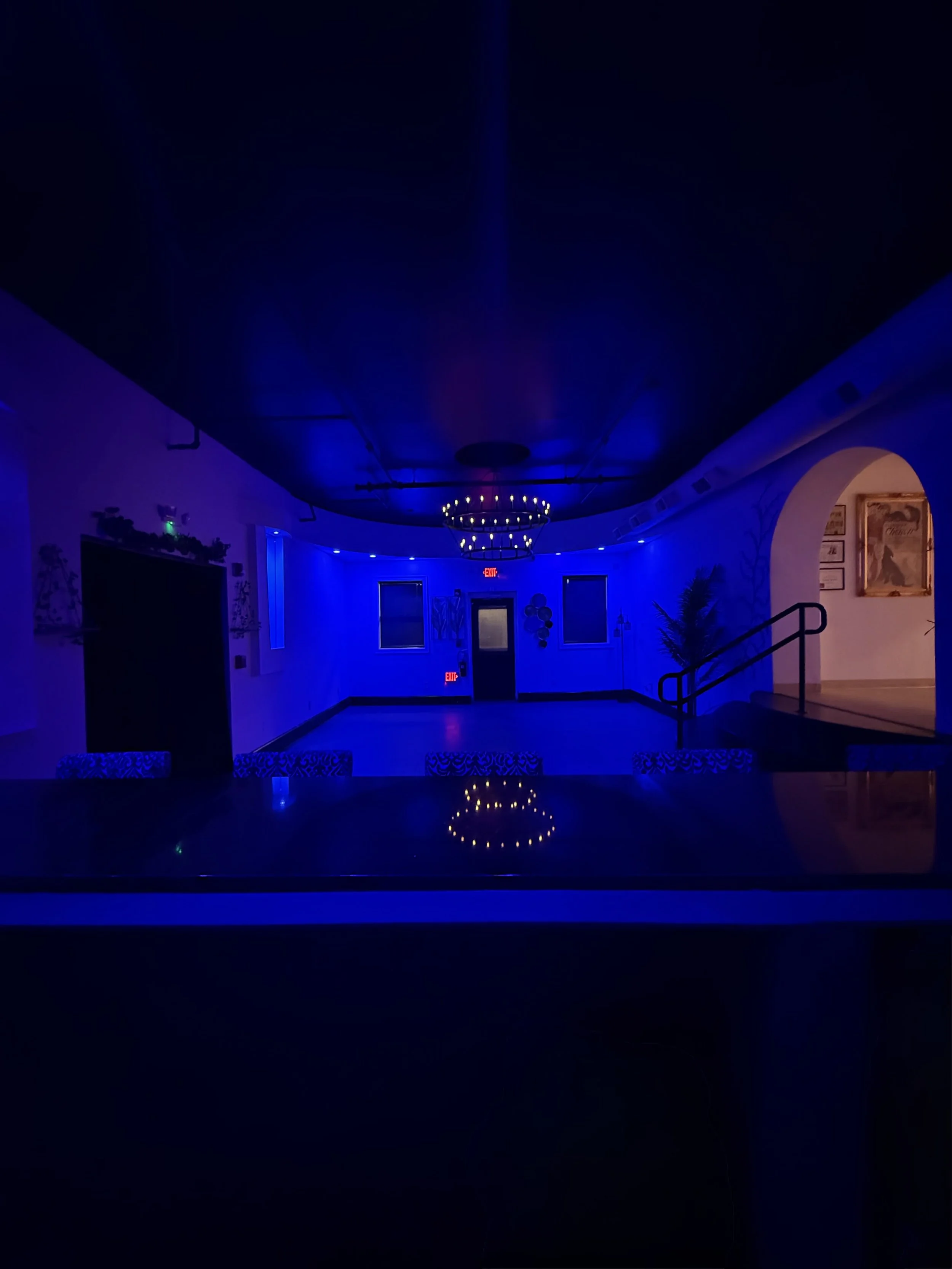 Dimly lit room with blue lighting, chandelier on ceiling, and artwork on walls.