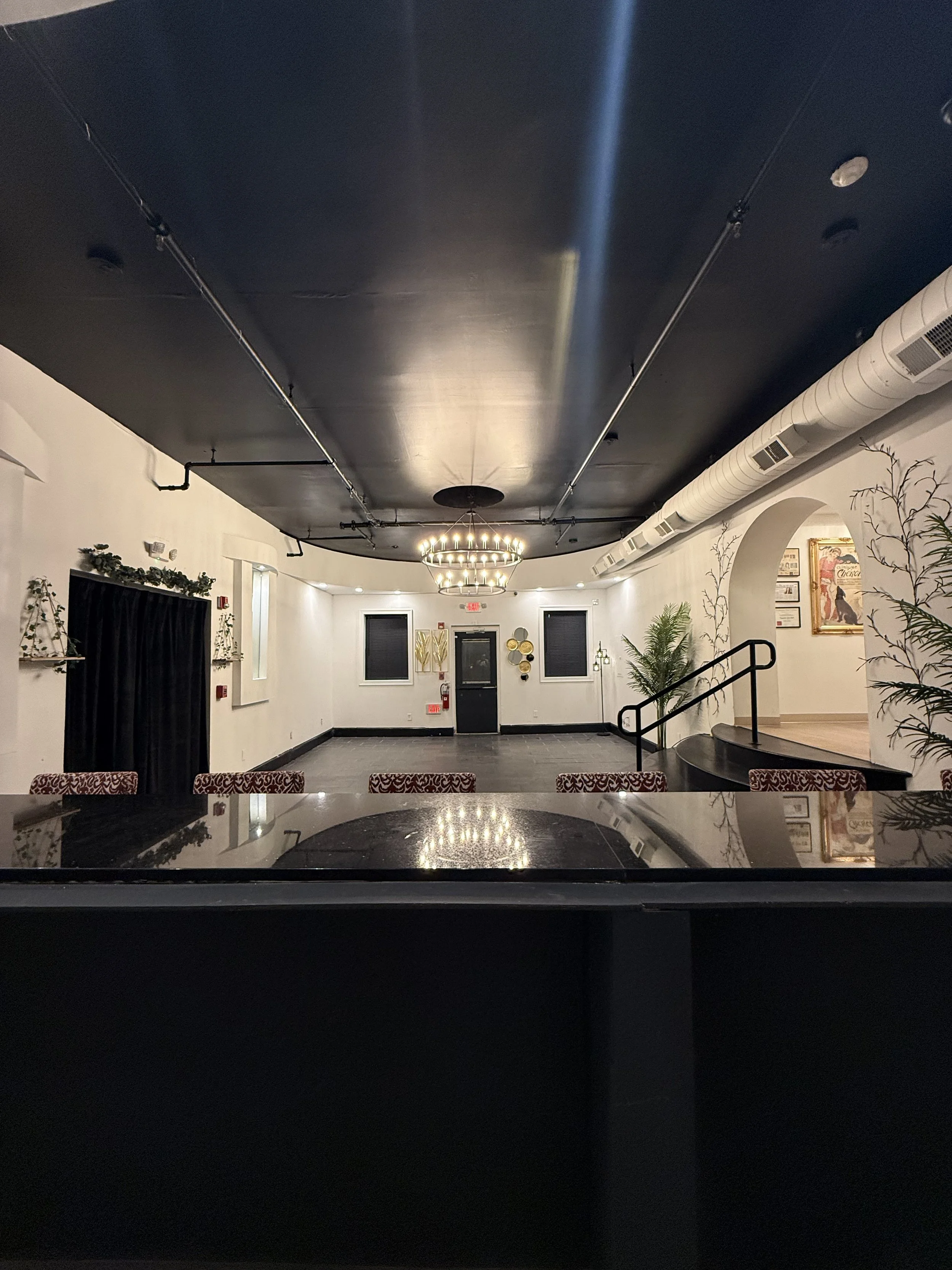 Empty event space with a black ceiling, chandelier, white walls, and framed artwork.