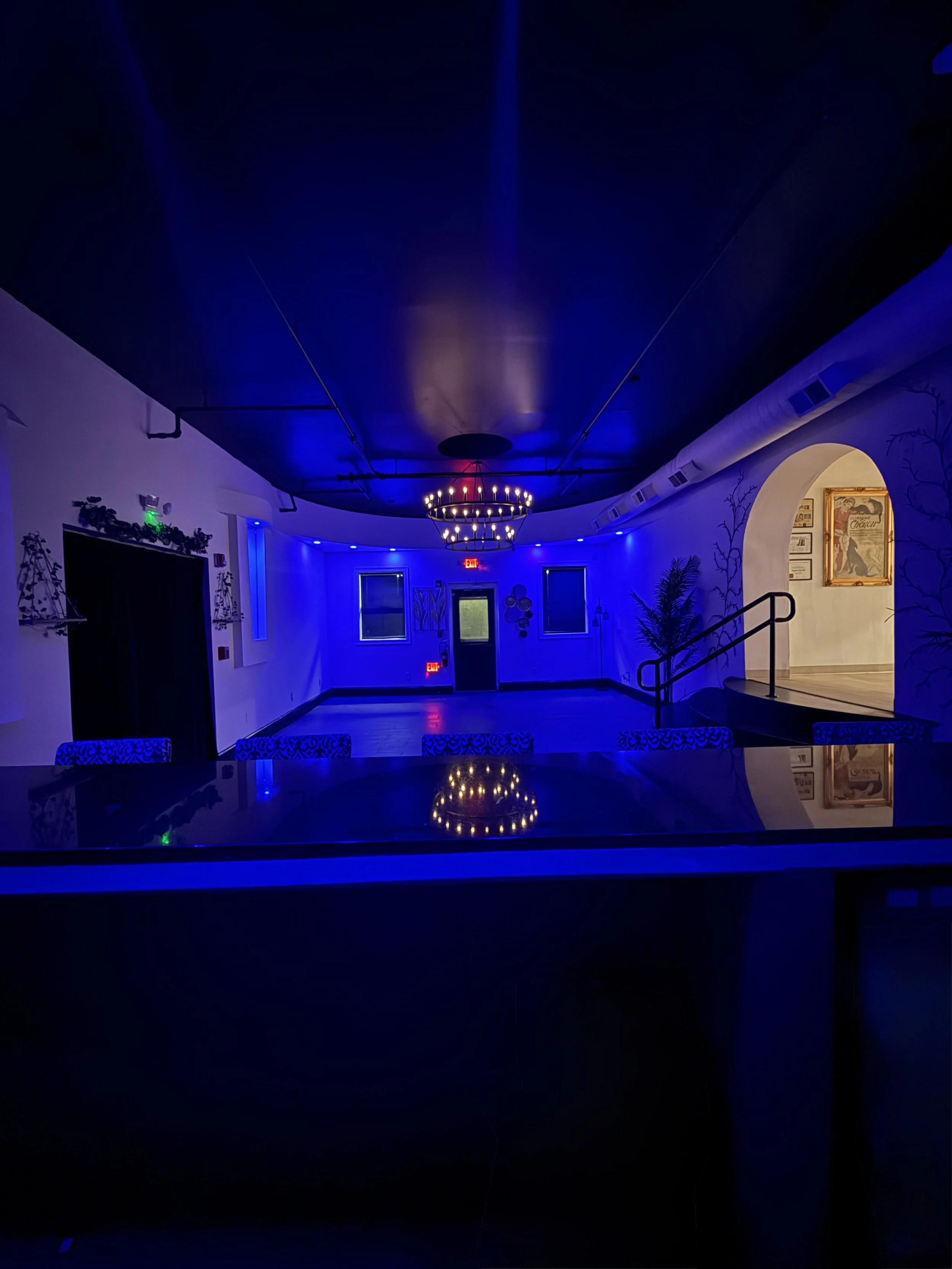 Indoor space illuminated with blue and purple lighting, featuring a chandelier, windows, and wall decorations.