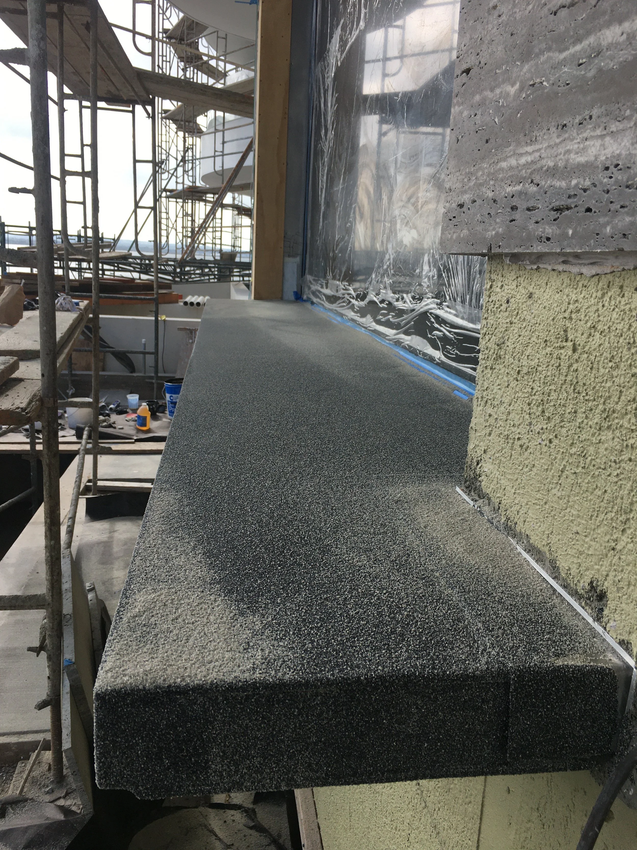 Construction site showing a newly installed black speckled countertop next to a yellow textured wall with some scaffolding and building materials in the background.