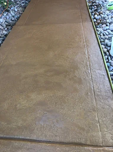 Concrete sidewalk with a strip of decorative rocks and a green garden hose on the side.