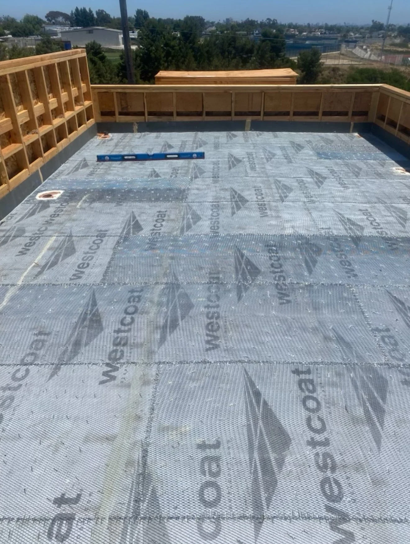 Construction site with a new rooftop deck under construction, showing a wooden railing and a black waterproof membrane with the Westercoast logo.