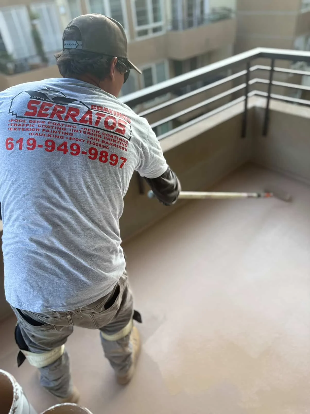 Worker on balcony applying a coating to the floor with a long-handled roller.