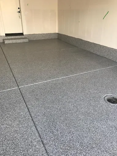 Empty garage with gray textured flooring, a drain in the corner, and a closed door on the back wall.