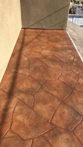 Outdoor concrete patio with a stamped and stained design, adjacent to a beige wall and a metal railing.