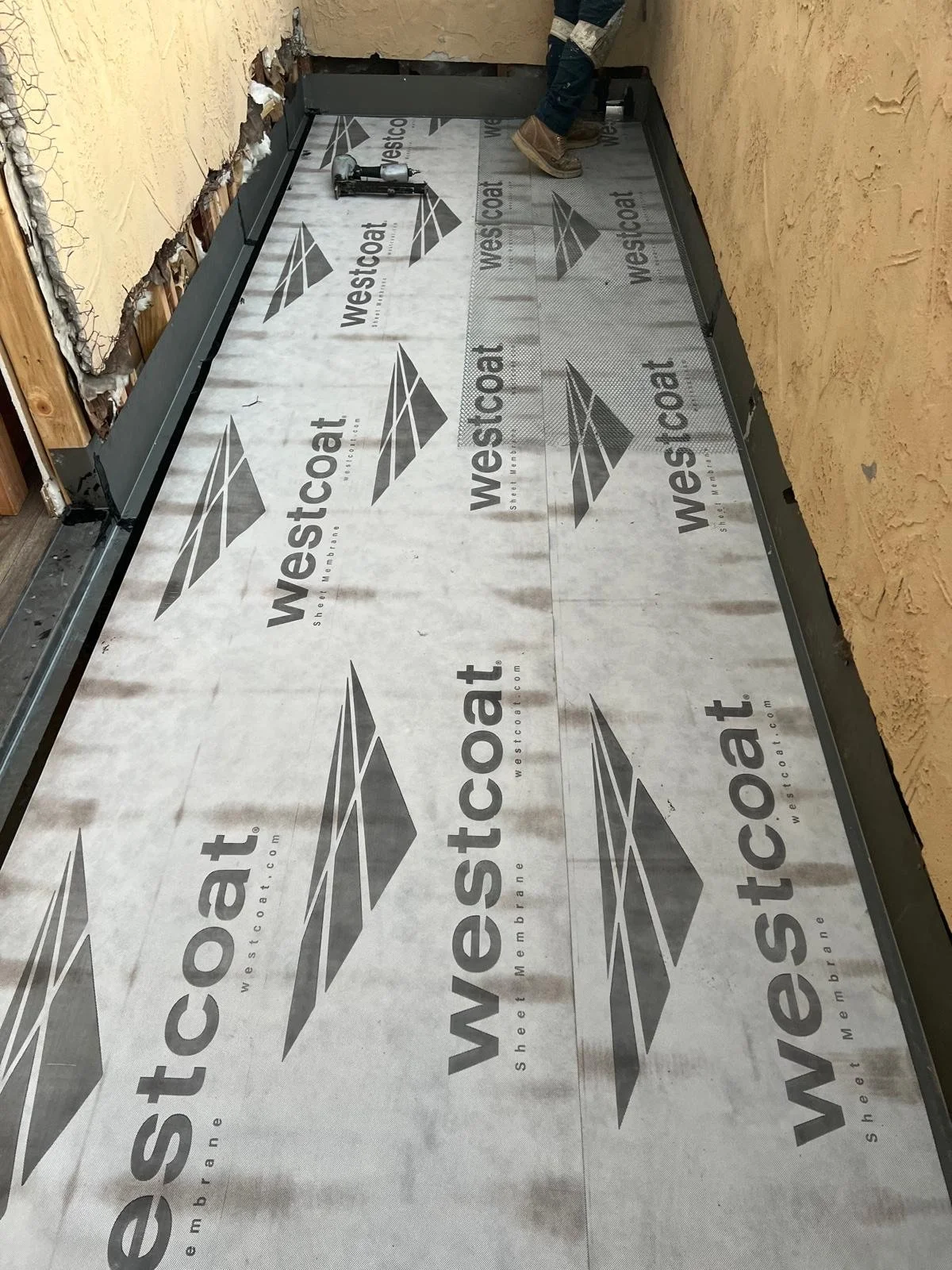 Construction site showing a floor with Westcoat branding and a person working with tools, with a partially finished wall.