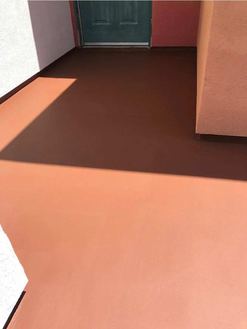A photo of a brown floor with a shadow cast from an unseen object and a green door in the background near a peach-colored wall.