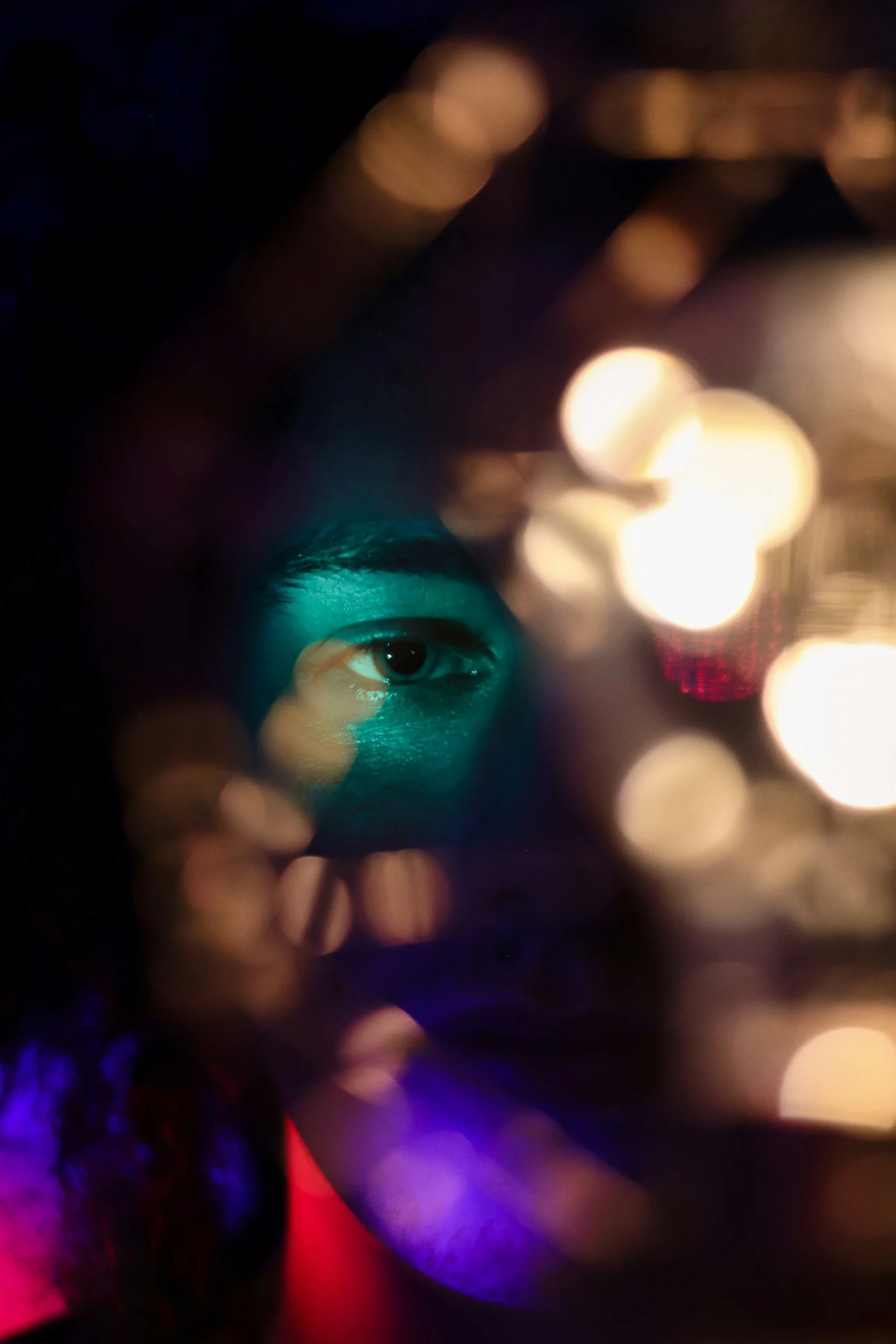 Close-up of a woman's face seen through out-of-focus colorful lights at night, with one eye in focus.