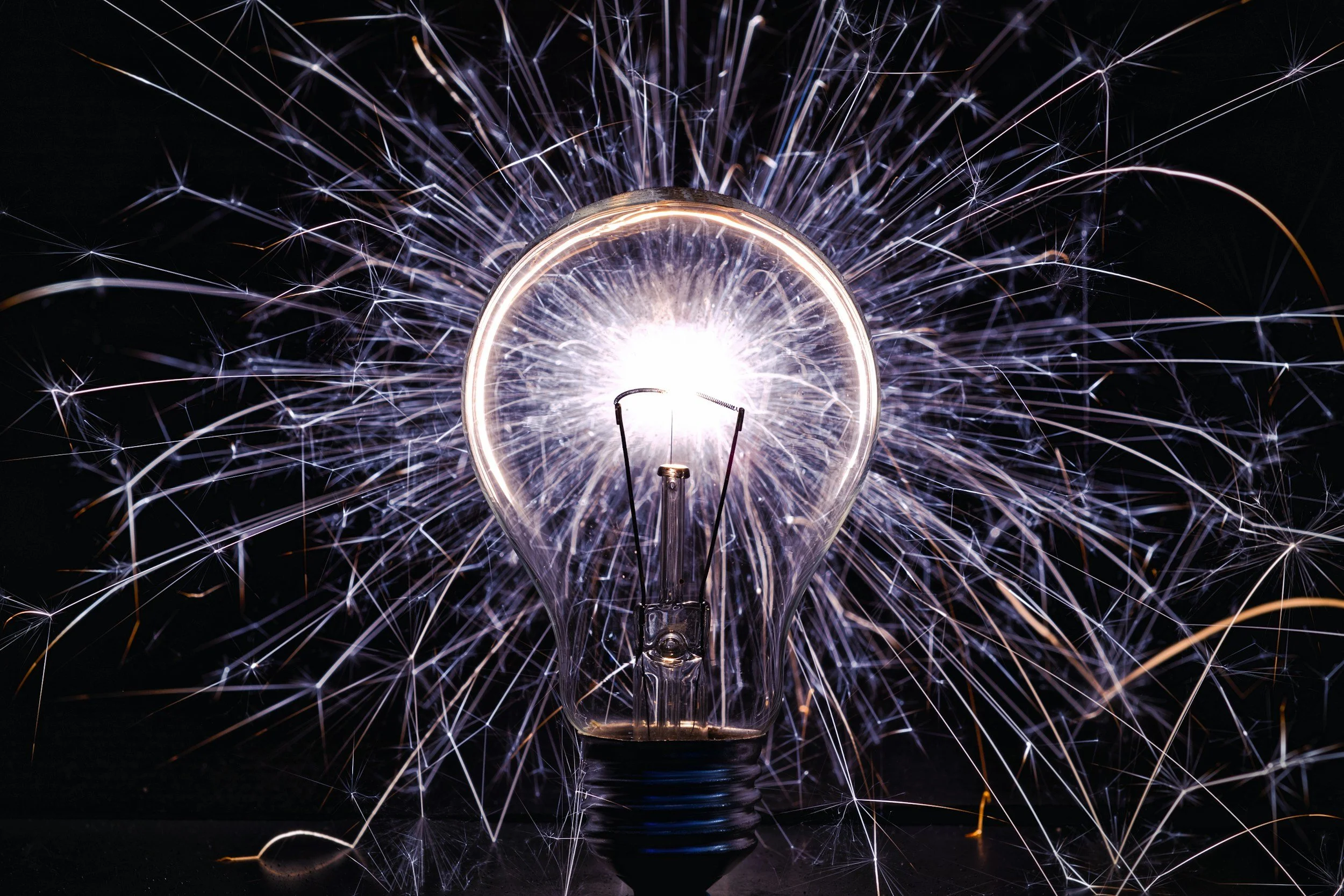 A lit light bulb surrounded by sparks and bright light.