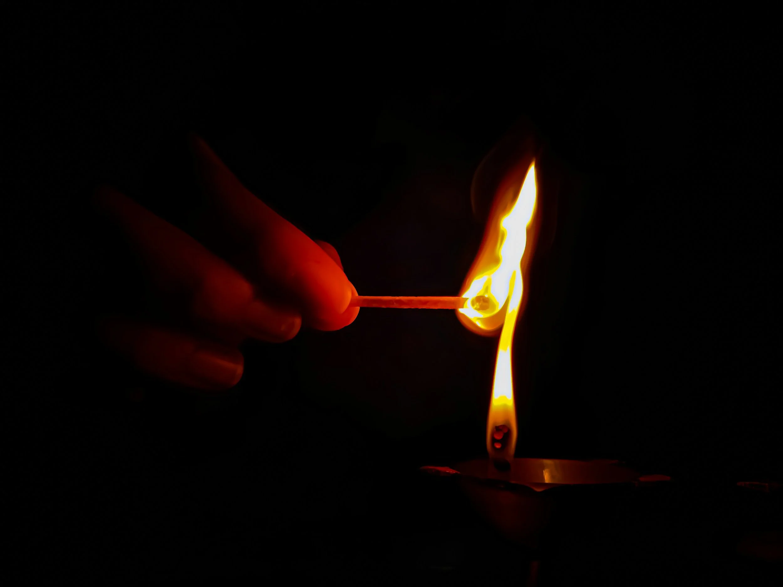 A person holding a matchstick and igniting a flame in complete darkness.