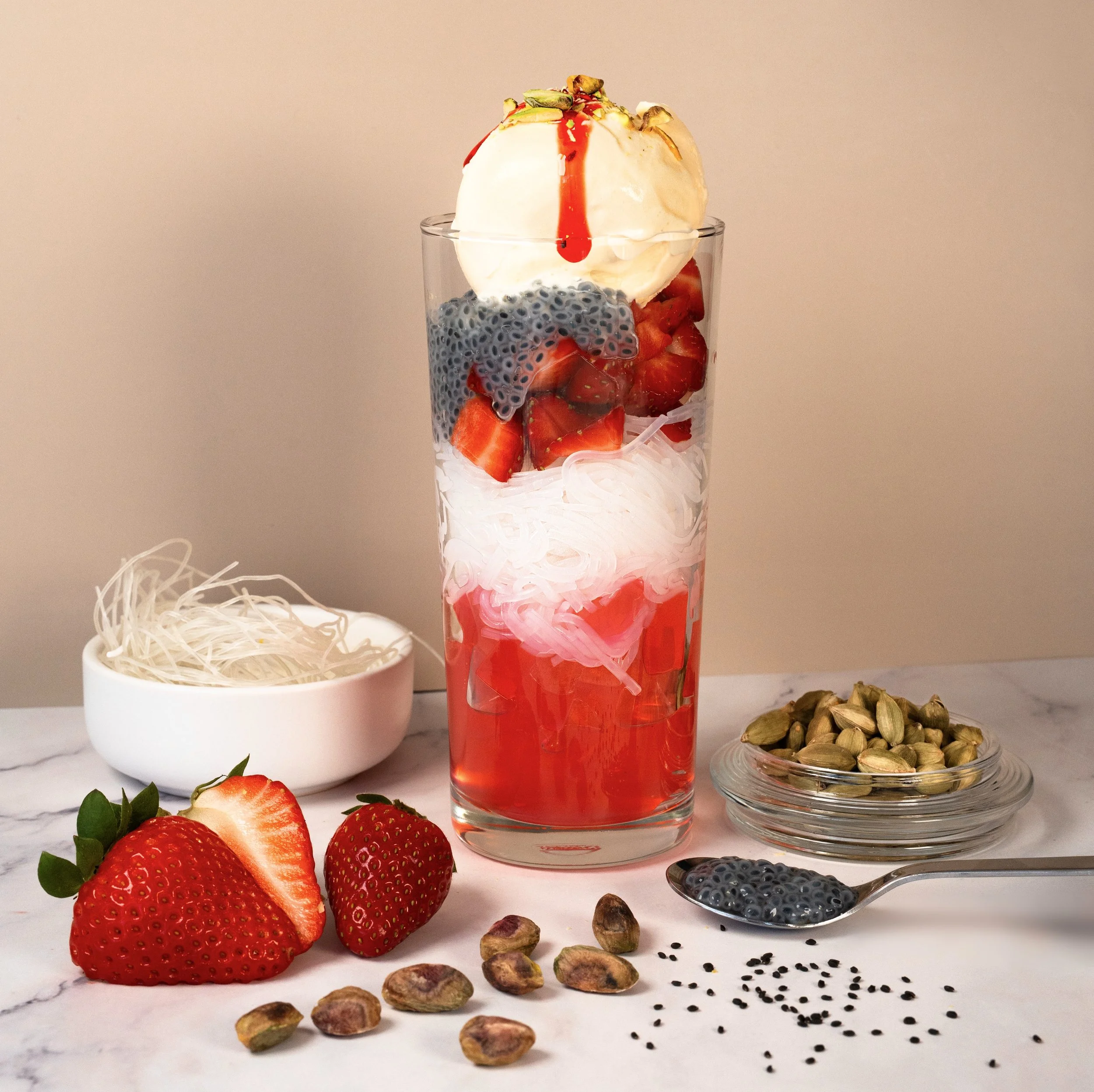 Falooda layered dessert with rose jelly, basil seeds and pistachios in a tall glass