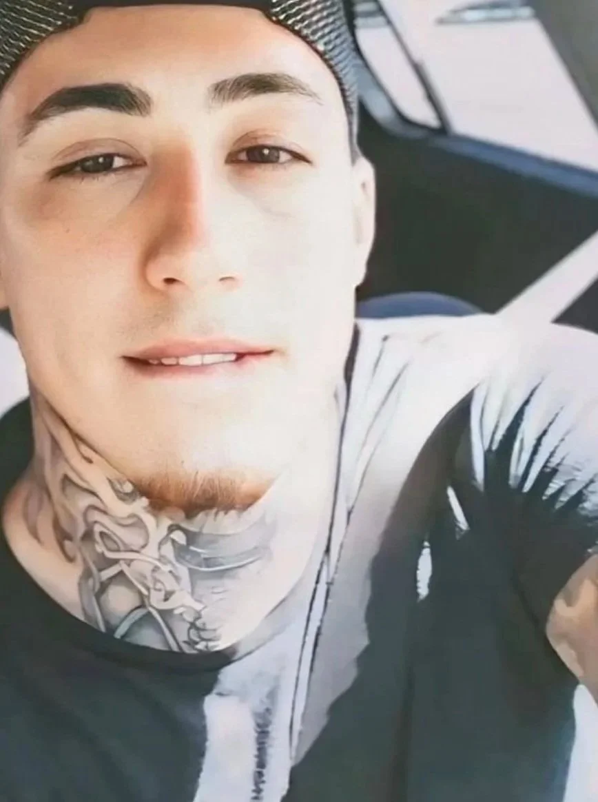 Close-up selfie of a young man with dark hair, tattoos on his neck, and wearing a cap, taken from an elevated angle.
