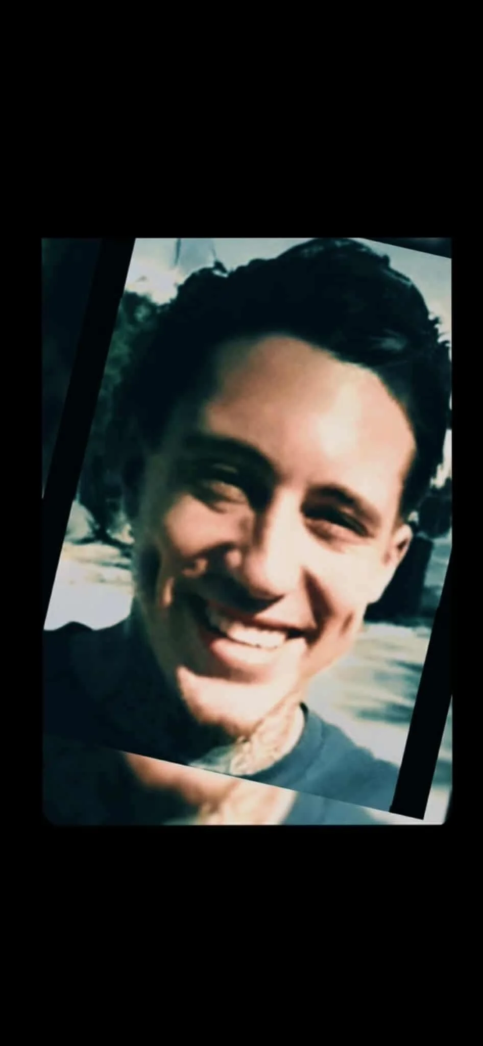 Young man smiling outdoors near a beach or body of water.