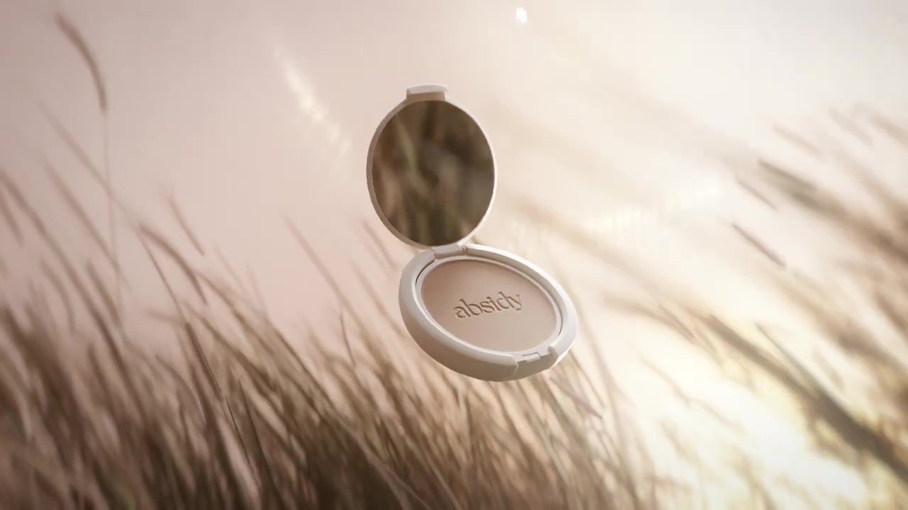 A compact mirror with the word "absity" on the inside, open and floating against a blurred natural background.
