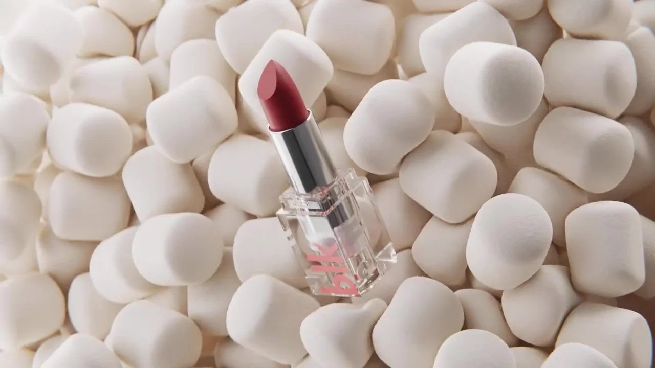 A pink lipstick in clear plastic packaging surrounded by white marshmallows.
