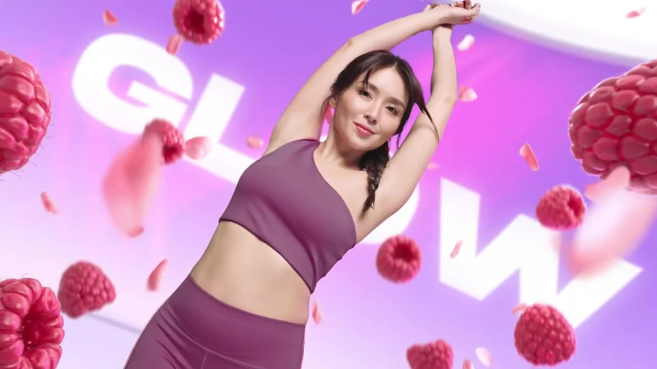 Woman in a purple sports bra and leggings stretching with a backdrop of floating berries and petals.