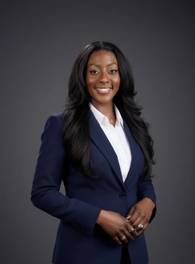 Professional woman smiling, wearing a gray blazer and white shirt, with long curly hair, against a dark gray background.