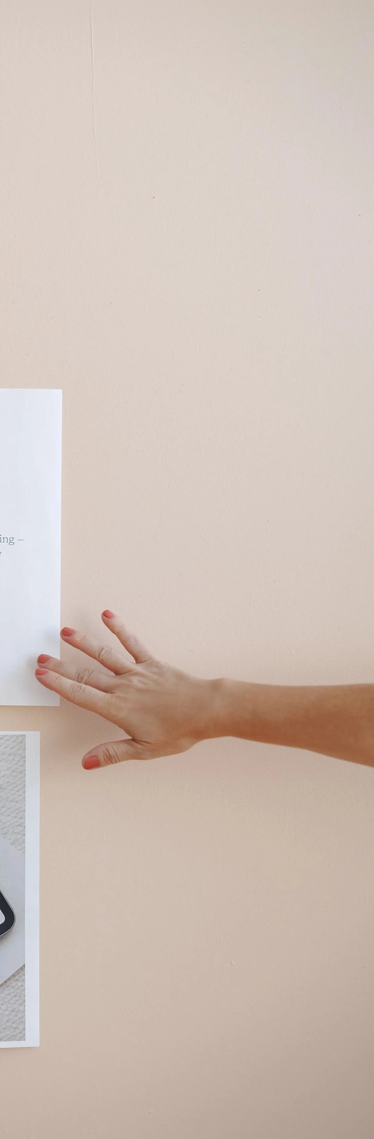 A person's arm and hand reaching outward, with the fingers extended, over a light beige wall with a piece of paper partially visible on the left side.