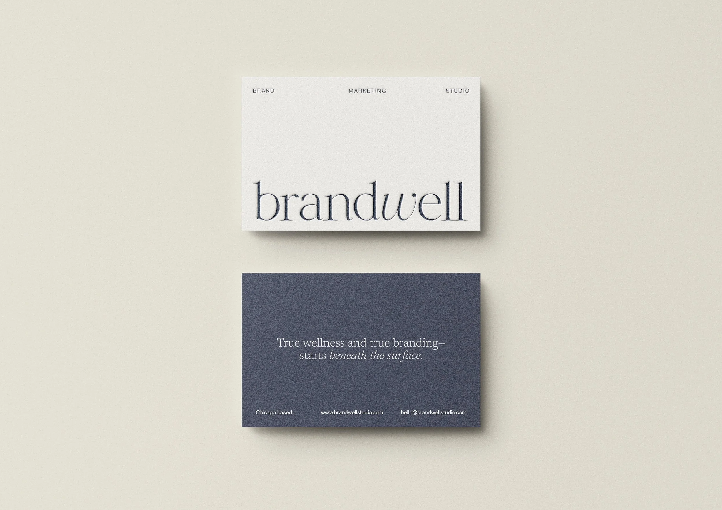 Minimalist branding business card design with a white card on top displaying the word 'brandwell' in large, elegant letters, and a dark blue card below with a tagline about wellness and branding, along with contact information.