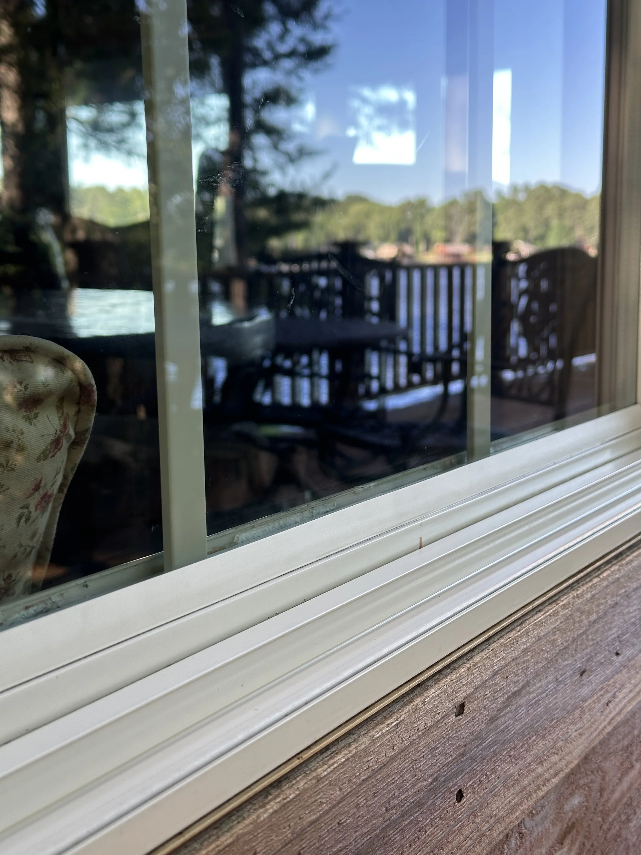 View through a window showing a wooden deck with chairs and trees in the background.
