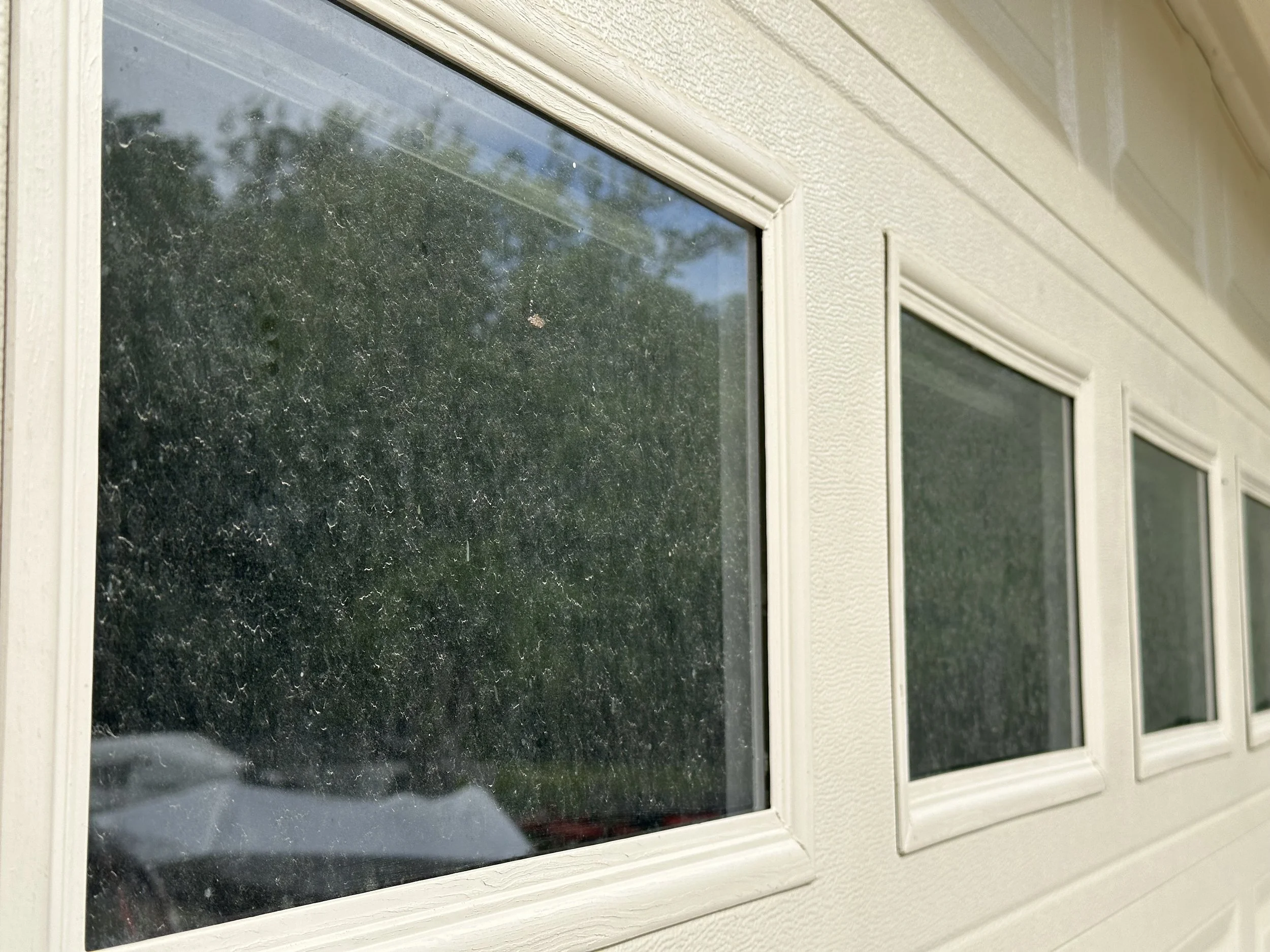 Close-up of a row of three small, rectangular windows on a beige wall, with the left window showing a reflection of trees and a car outside.