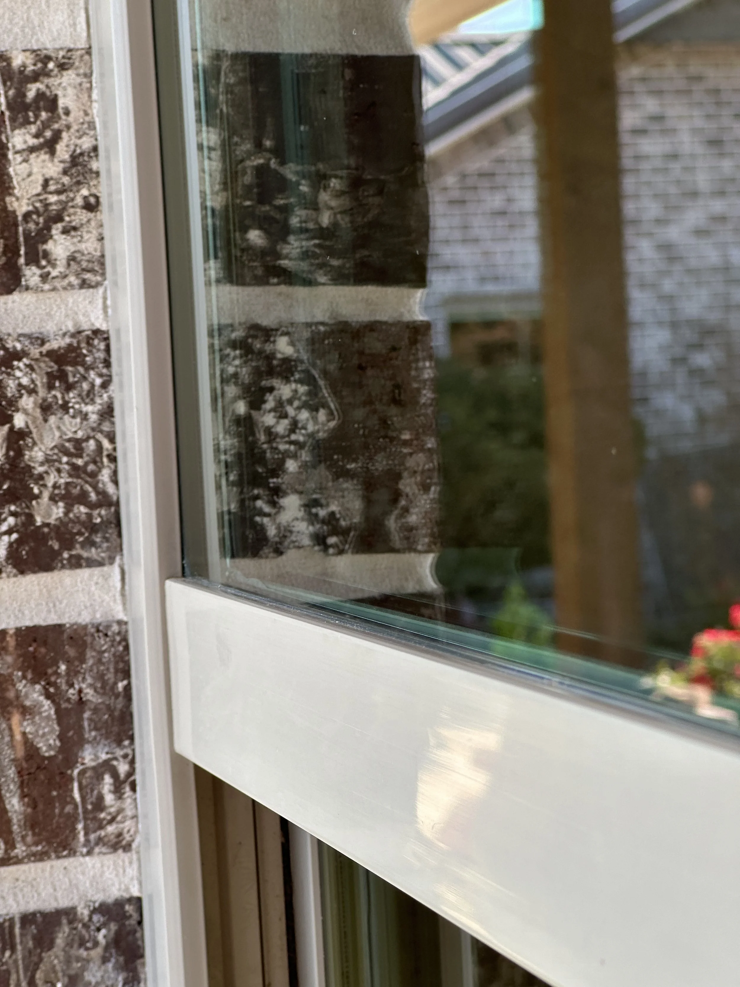 Close-up of a window with brick wall outside, showing a reflection of a person capturing the photo.