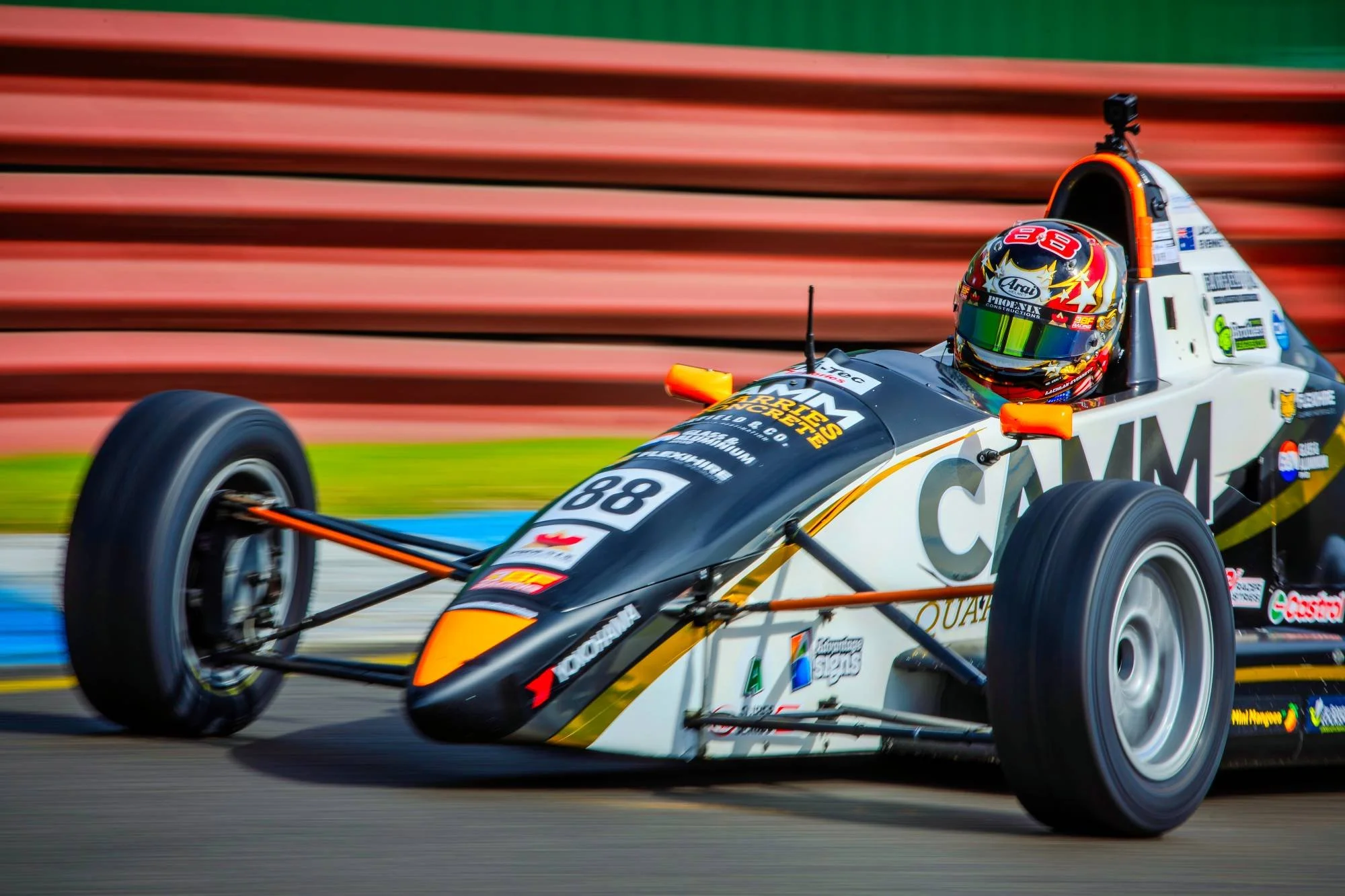 A race car on a racetrack with a driver wearing a helmet, moving quickly.