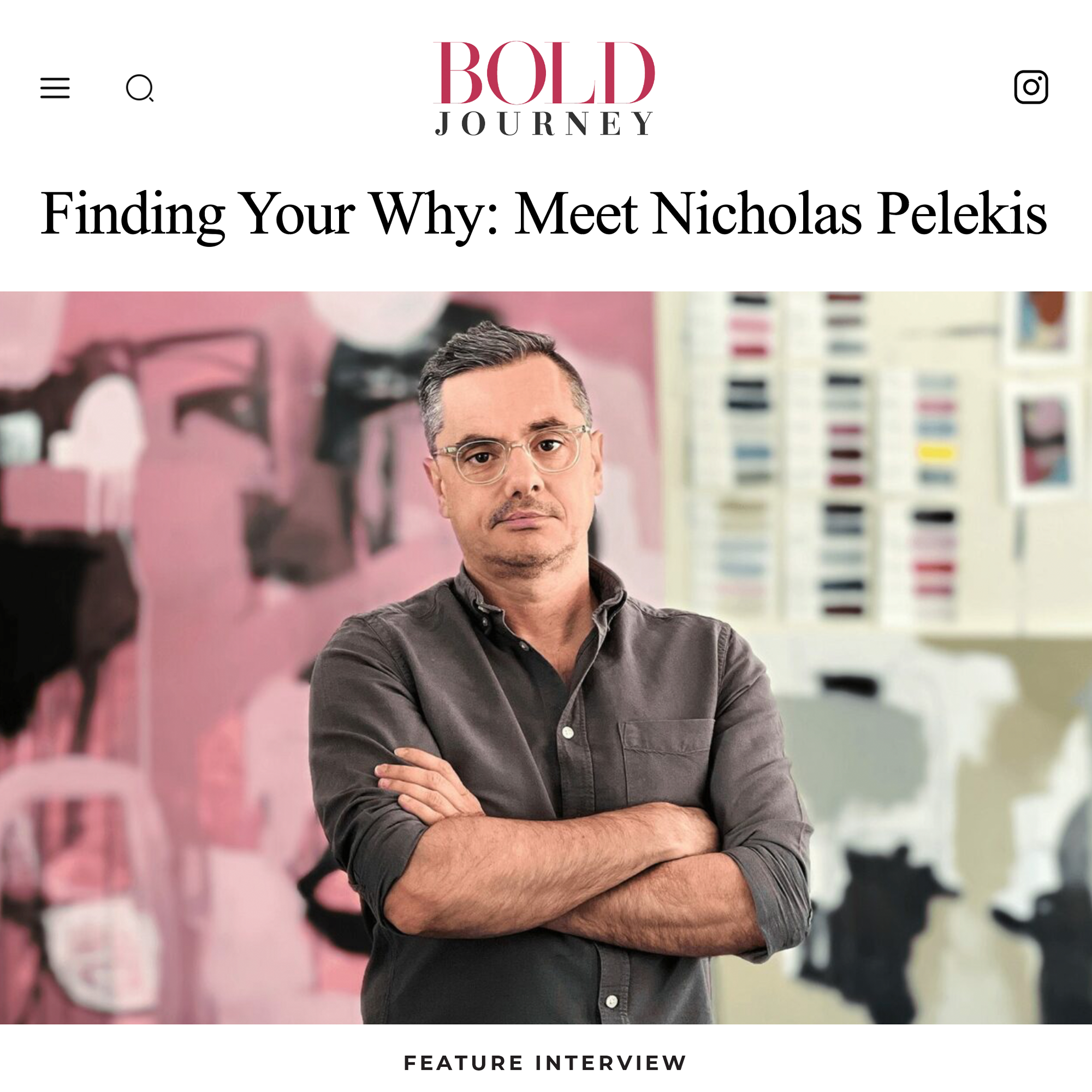 A man with short dark hair, glasses, and a gray button-up shirt with rolled-up sleeves, standing with arms crossed in front of a colorful abstract mural and a wall of fabric swatches.