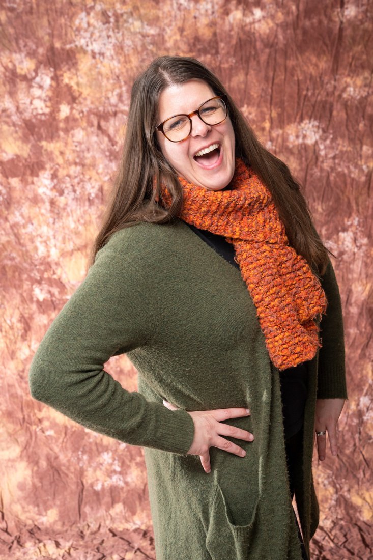 Monica Vasquez, Portland real estate broker, wearing a green cardigan and orange scarf, posing in front of an autumn backdrop.