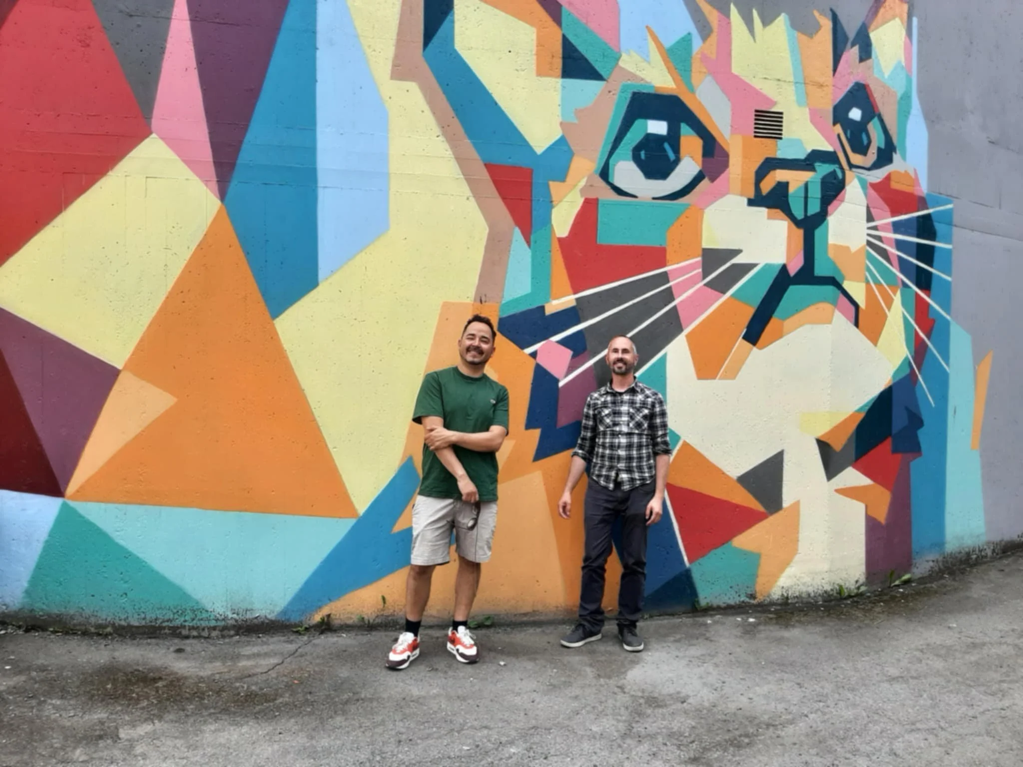 Två män står framför en färgglad graffiti av en tiger på en vägg.