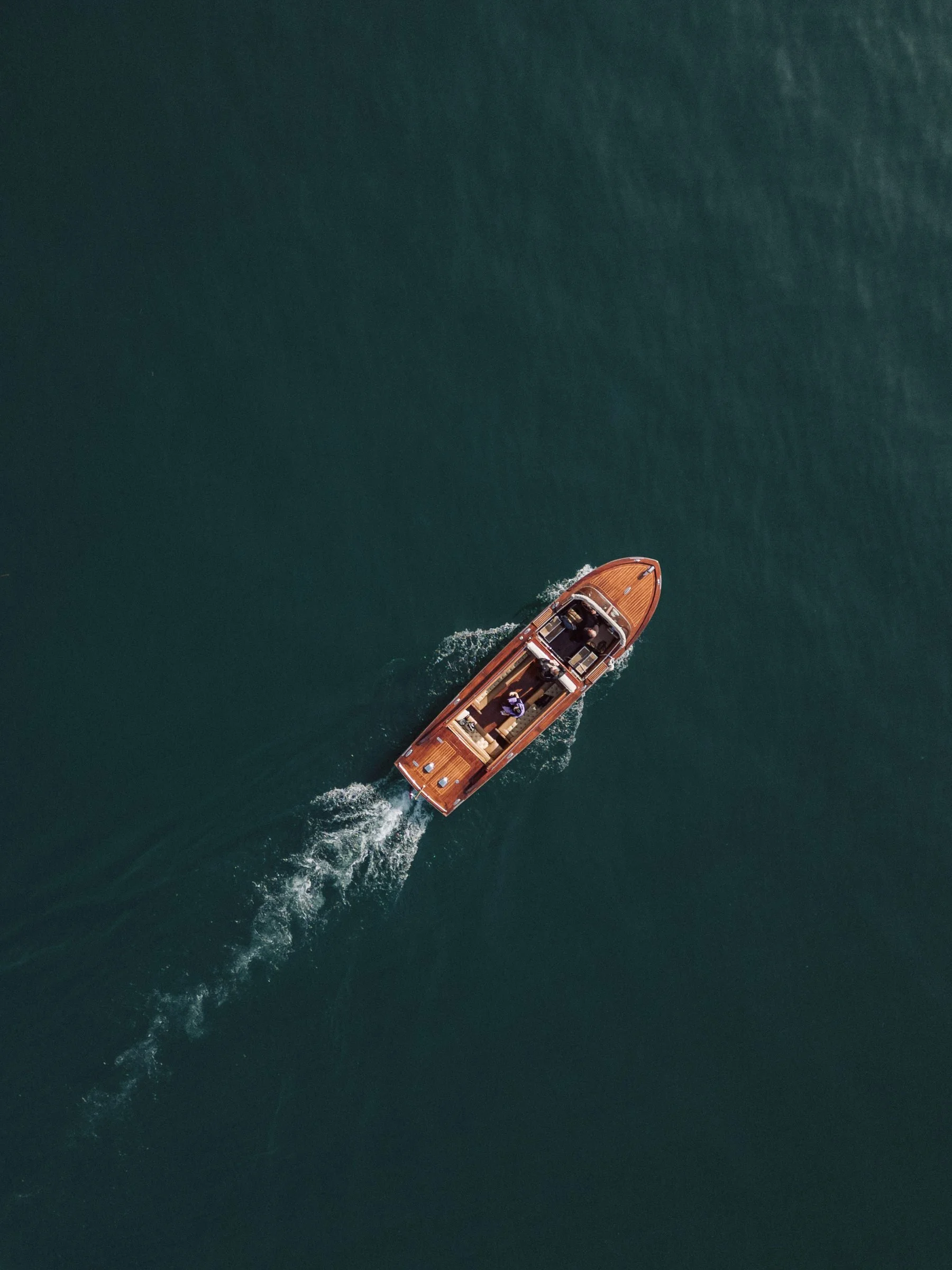 Aerial view of a wooden yacht boat sailing on dark green water, leaving a trail behind.