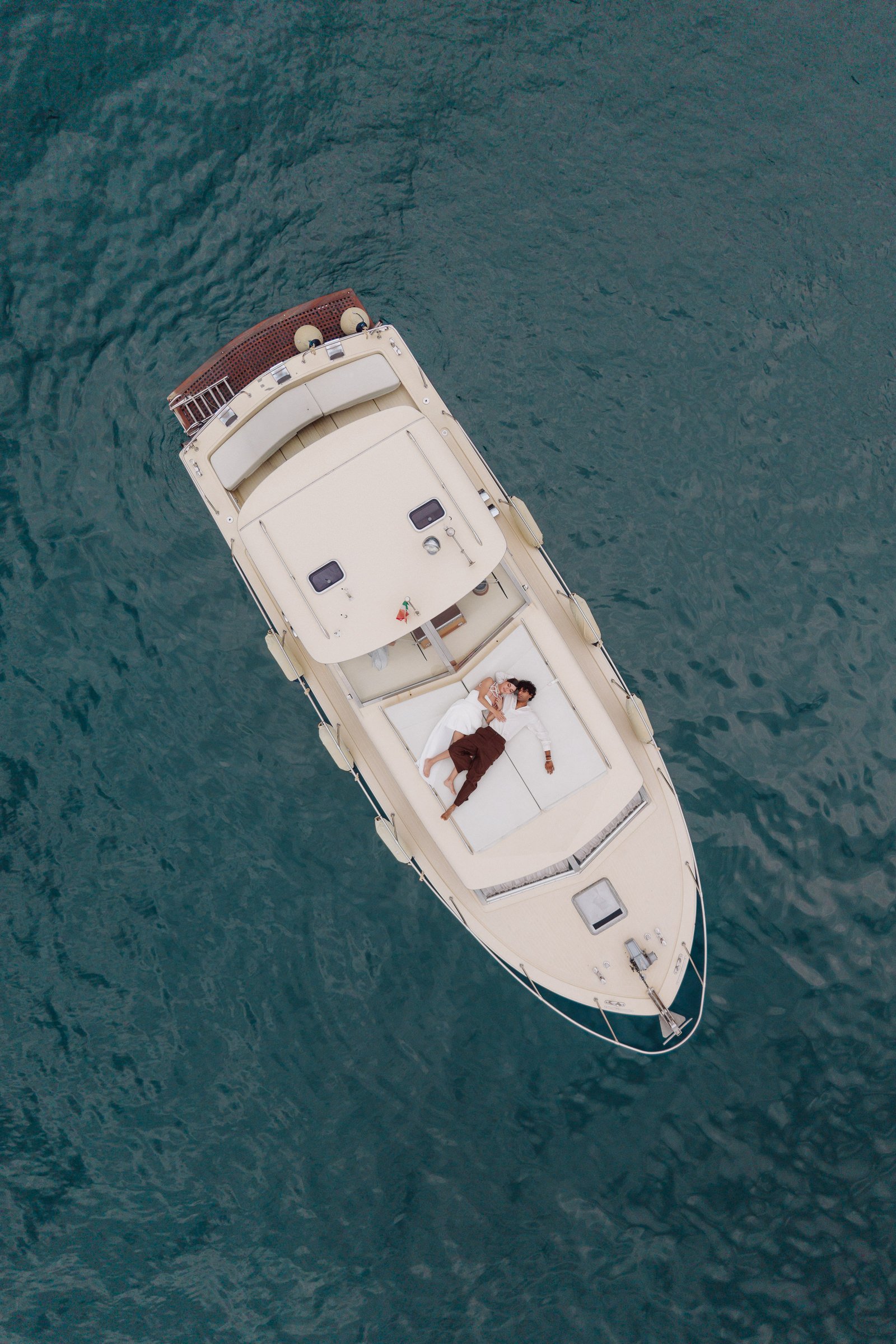 Aerial view of a boat with people lying on deck, floating on the water.