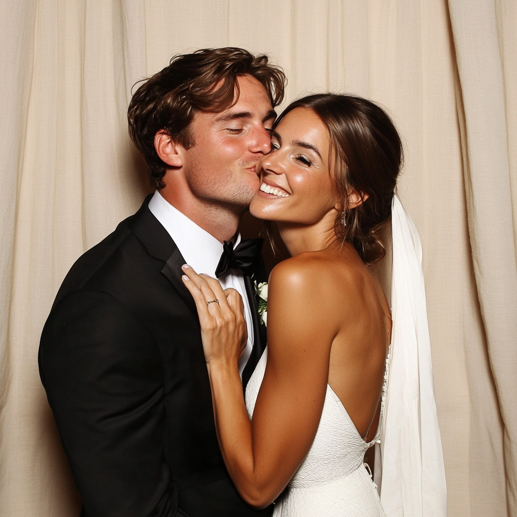 Happy bride and groom on their wedding day, embracing and smiling in front of a light-colored curtain.