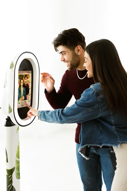 A man and woman using a photo booth with a touchscreen display, taking a selfie together.