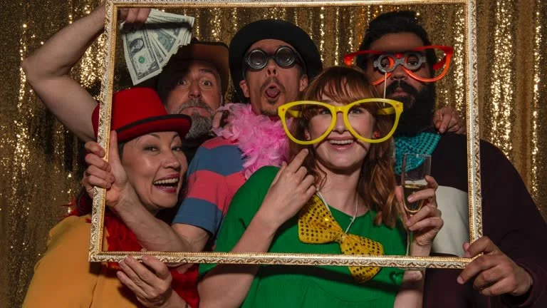 Wedding photo booth setup with digital screens displaying photos of a bride and groom, surrounded by white floral arrangements on a table.