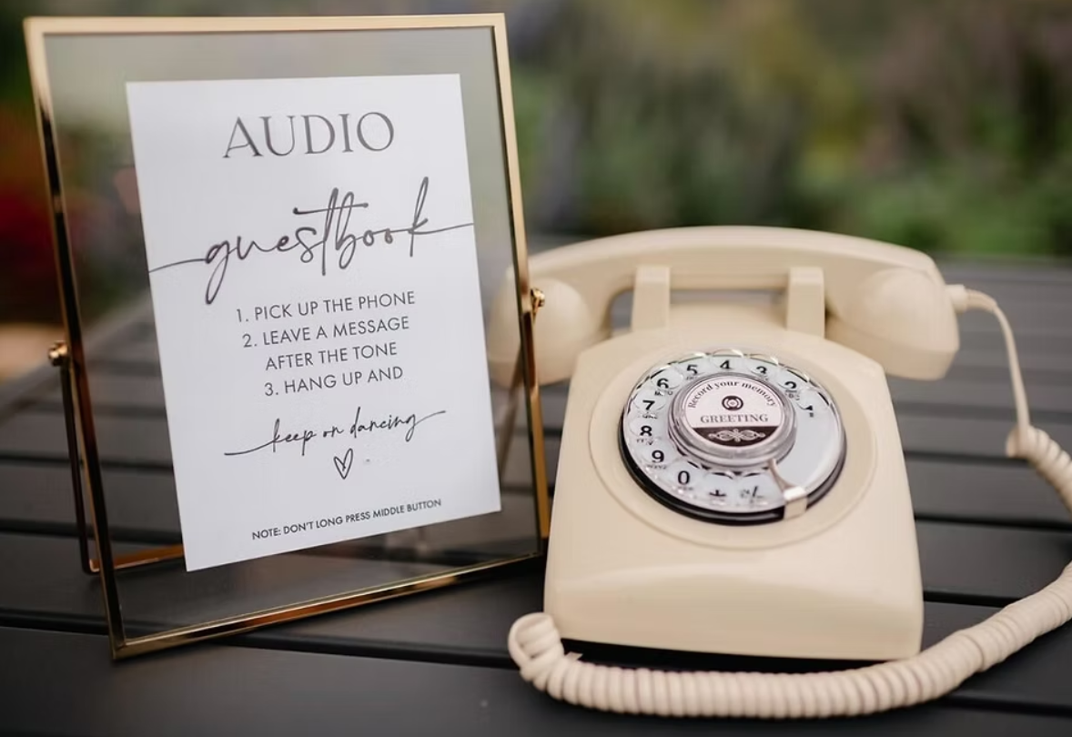 Wedding photo booth setup with digital screens displaying photos of a bride and groom, surrounded by white floral arrangements on a table.